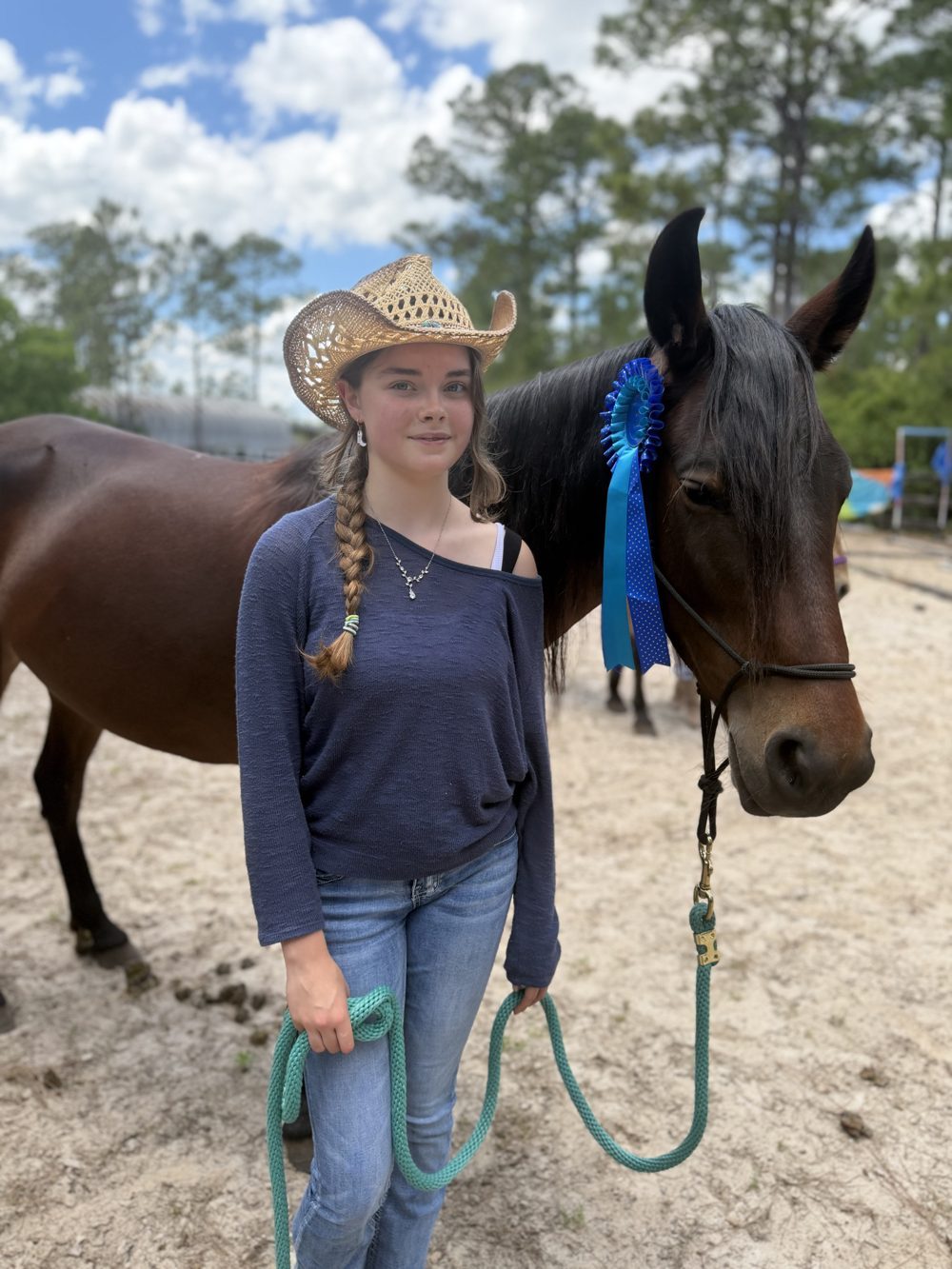 A young woman in a cowboy hat stands with a dark bay horse at The Refuge