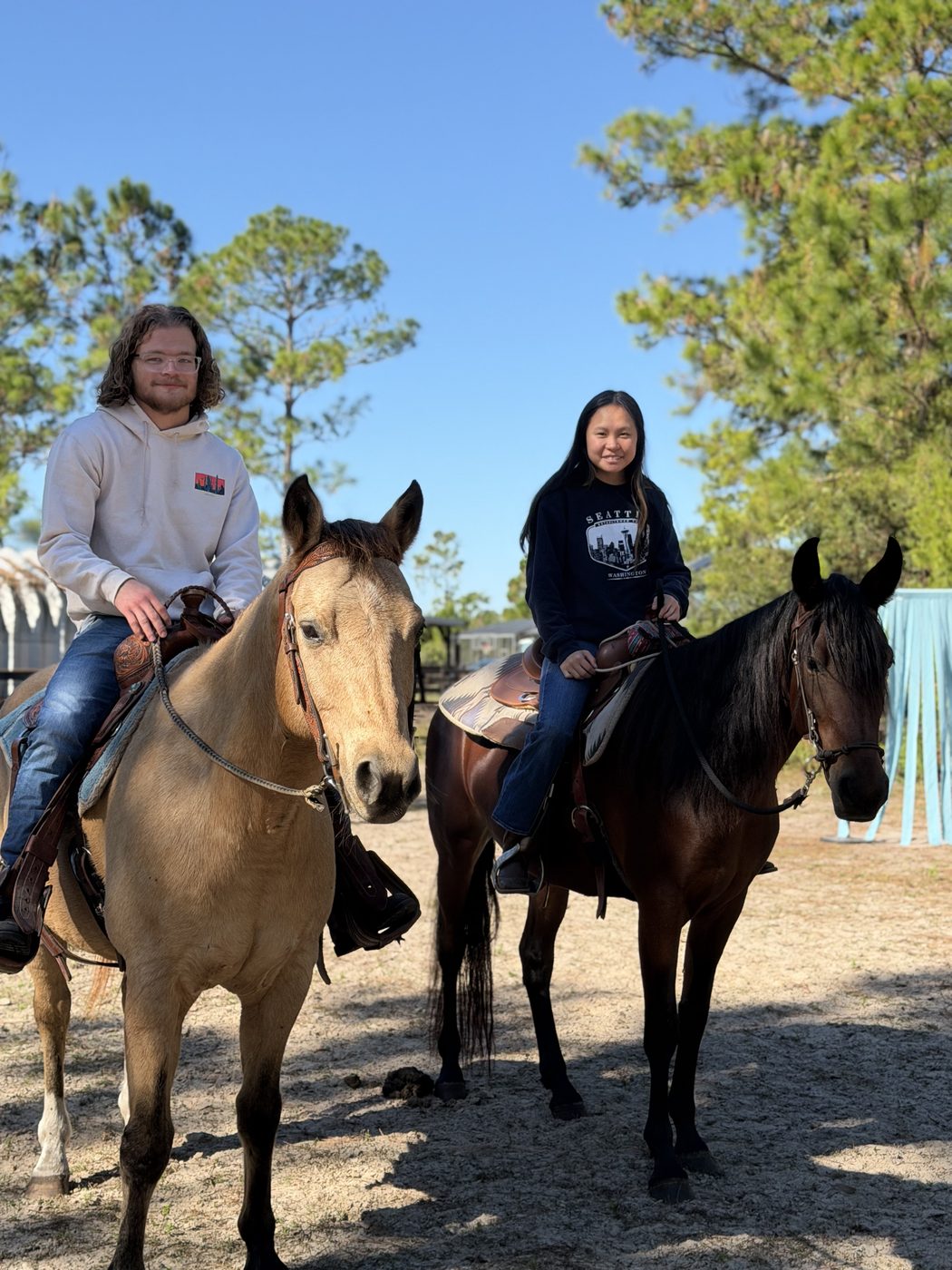 Two smiling riders on a buckskin and a dark bay horse